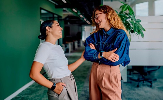 Två kvinnor pratar glatt i kontorsmiljö