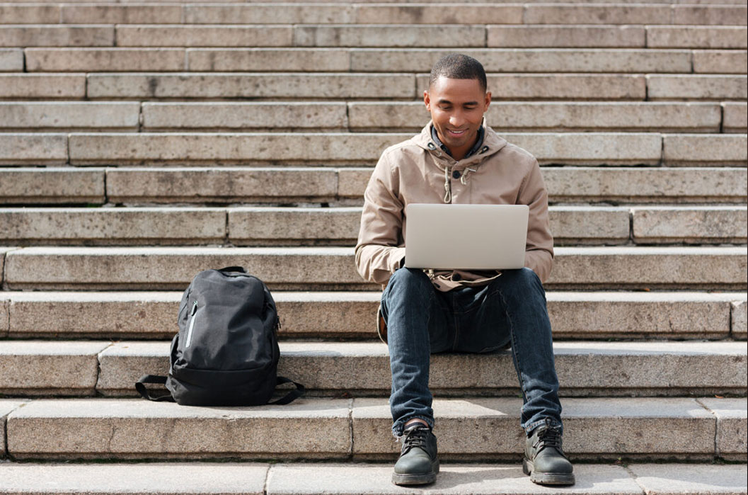 Man sitter i en trappa med en bärbar dator i knät.